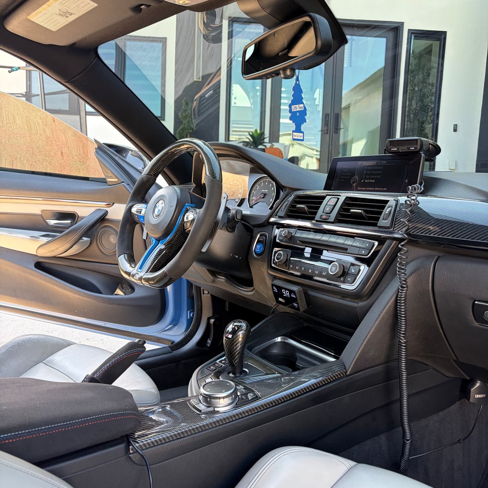 Detailed driver cockpit of the light blue BMW M4 with carbon trim and white leather seats
