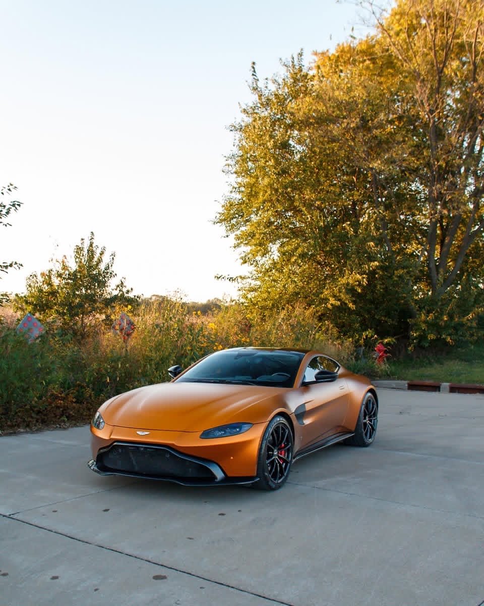 Matte orange Aston Martin Vantage front three-quarter in front of trees after an exterior detail in Altoona