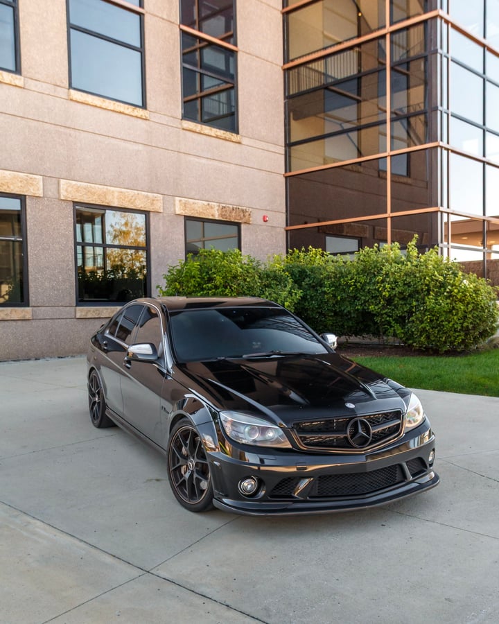 Black Mercedes sedan in front of an office building photographed by Kenny