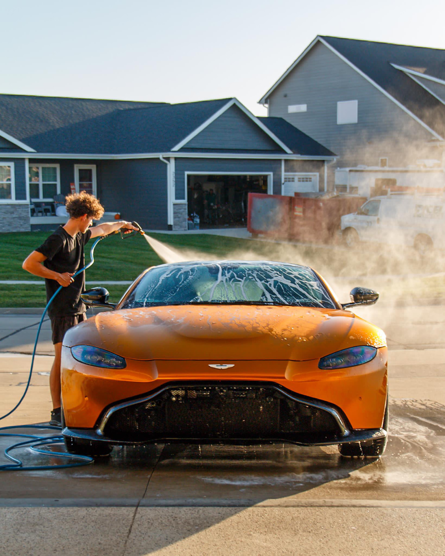 Matte orange Aston Martin Vantage Jake rinsing it in an Altoona driveway after an exterior detail in Altoona