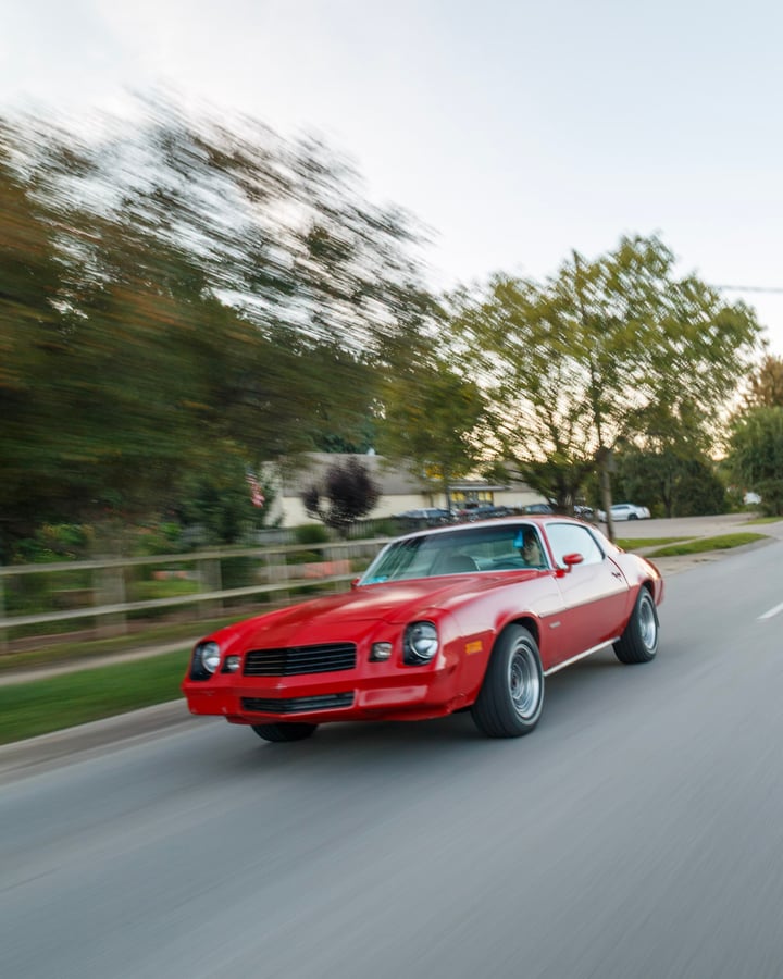 Red classic Camaro rolling shot by Kenny on a tree-lined road