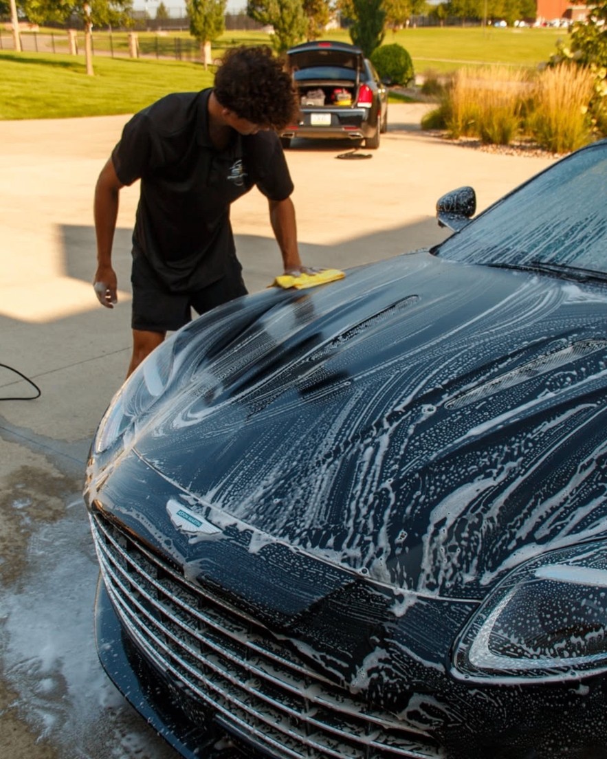 Jake hand washing a foam-covered Aston Martin during an exterior detail in the Des Moines metro